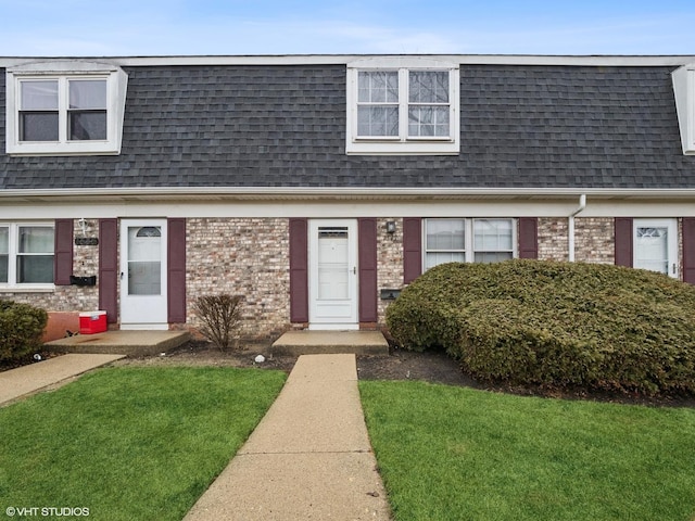 view of front of property with brick siding, a front yard, mansard roof, and roof with shingles