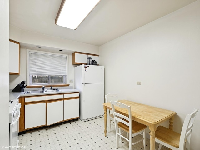 kitchen with light floors, light countertops, freestanding refrigerator, a sink, and range