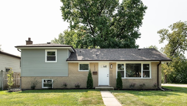 split level home featuring a front lawn, a chimney, fence, and brick siding