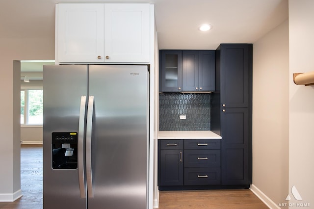 kitchen featuring stainless steel fridge, light countertops, light wood-type flooring, white cabinetry, and backsplash