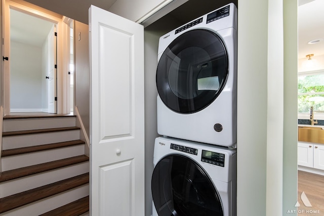 clothes washing area featuring light wood-type flooring, stacked washer / dryer, laundry area, and a sink