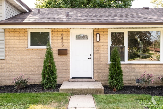 doorway to property featuring a shingled roof, crawl space, and brick siding