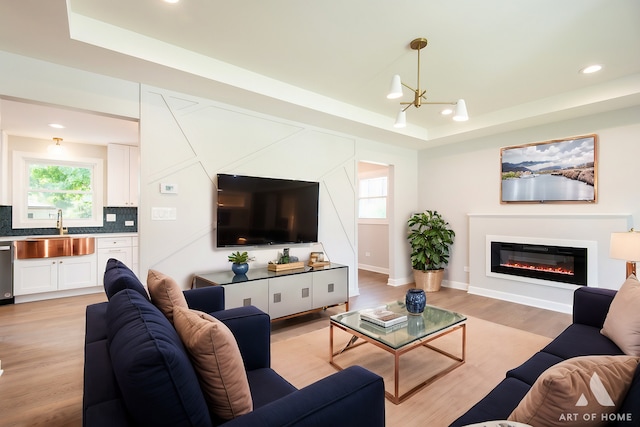 living area featuring a tray ceiling, plenty of natural light, and a glass covered fireplace