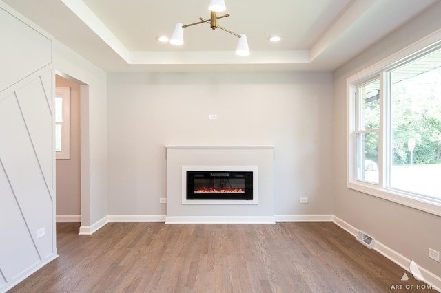 unfurnished living room with wood finished floors, a raised ceiling, visible vents, and baseboards