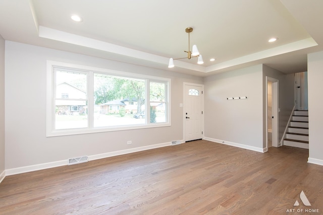 foyer entrance with a tray ceiling, light wood finished floors, recessed lighting, visible vents, and baseboards