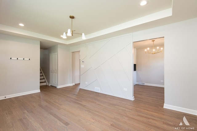 unfurnished room featuring a chandelier, recessed lighting, wood finished floors, baseboards, and a tray ceiling