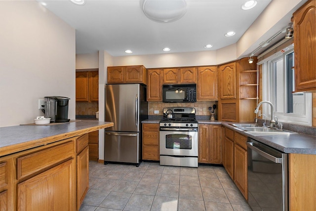 kitchen featuring brown cabinetry, a sink, appliances with stainless steel finishes, dark countertops, and tasteful backsplash