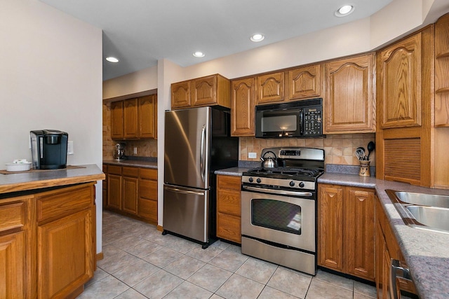 kitchen with light tile patterned floors, backsplash, appliances with stainless steel finishes, and brown cabinetry