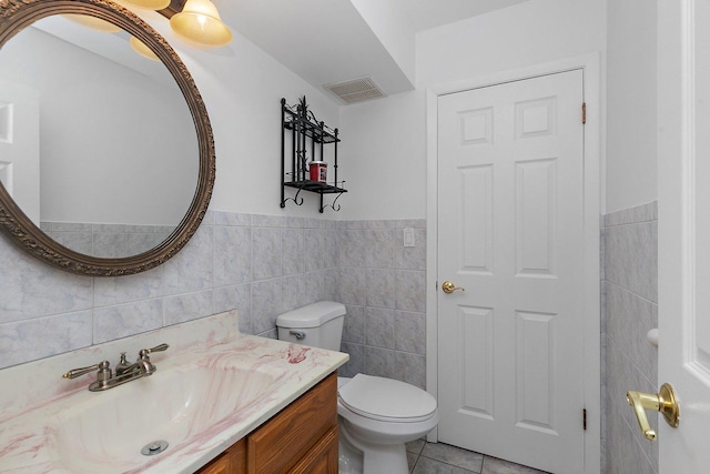 half bath with tile patterned flooring, visible vents, toilet, vanity, and tile walls