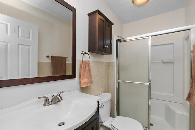 full bathroom with vanity, a wainscoted wall, a stall shower, tile walls, and toilet