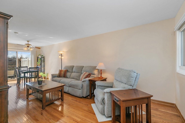 living area featuring baseboards, light wood-type flooring, and ceiling fan