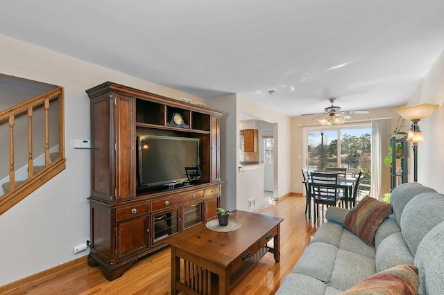 living area featuring light wood-style flooring, baseboards, stairs, and a ceiling fan