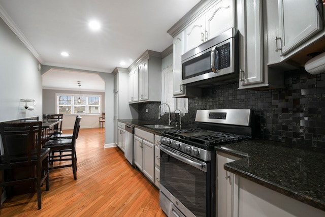 kitchen with a sink, light wood-style floors, appliances with stainless steel finishes, tasteful backsplash, and crown molding