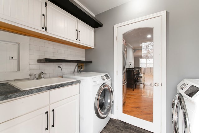 clothes washing area featuring a sink, baseboards, cabinet space, washer and clothes dryer, and dark wood finished floors