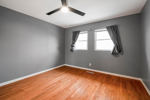 empty room with ceiling fan, wood-type flooring, visible vents, and baseboards