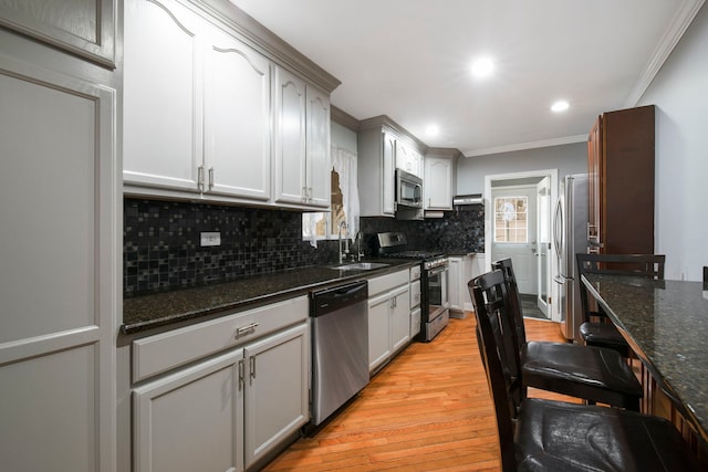 kitchen with light wood-style flooring, stainless steel appliances, a sink, backsplash, and crown molding