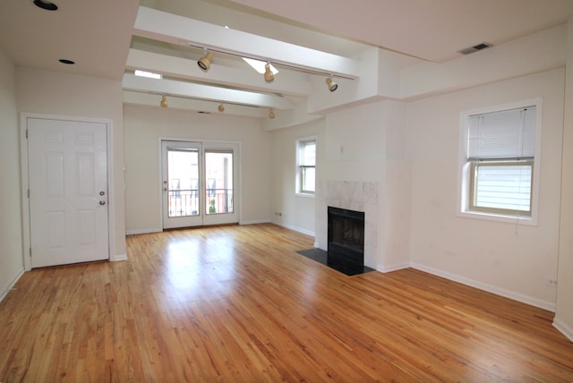 unfurnished living room with light wood finished floors, baseboards, visible vents, a tiled fireplace, and track lighting