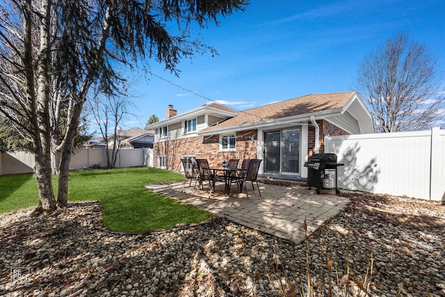 rear view of property with a lawn, a patio, a fenced backyard, a chimney, and brick siding