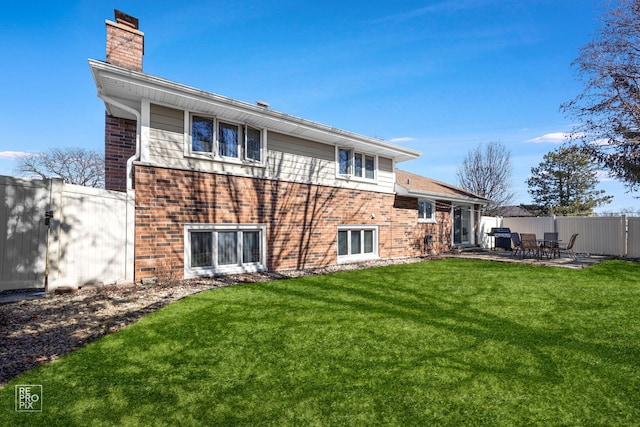 back of house with brick siding, fence, a yard, a chimney, and a patio area