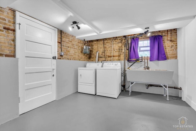 laundry area featuring laundry area, brick wall, separate washer and dryer, and a sink