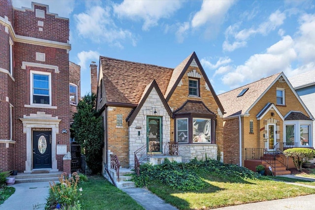 english style home featuring stone siding, brick siding, and a shingled roof