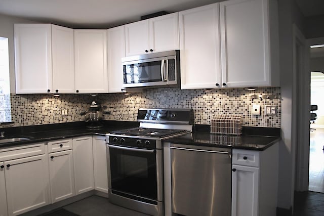 kitchen with stainless steel appliances, dark tile patterned flooring, white cabinetry, and decorative backsplash