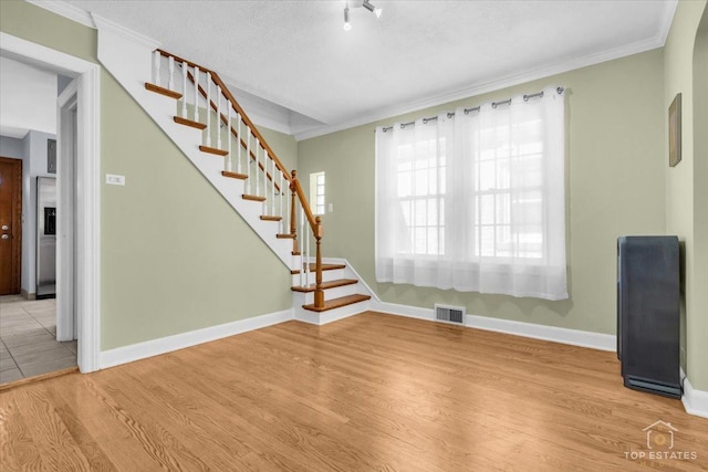 unfurnished living room with visible vents, ornamental molding, light wood-type flooring, baseboards, and stairs