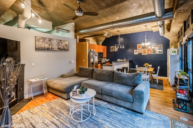 living room with baseboards, wood finished floors, and ceiling fan with notable chandelier