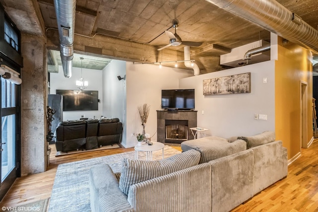 living area featuring ceiling fan with notable chandelier, a tiled fireplace, and wood finished floors