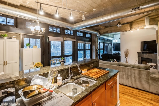 kitchen featuring a chandelier, a sink, light wood-style floors, dark stone counters, and brown cabinetry