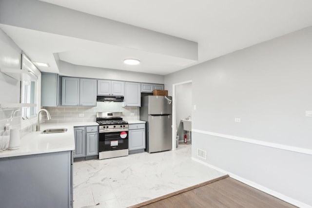 kitchen featuring appliances with stainless steel finishes, a sink, decorative backsplash, and gray cabinetry