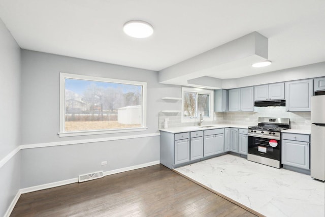 kitchen with under cabinet range hood, gray cabinetry, visible vents, stainless steel gas stove, and tasteful backsplash