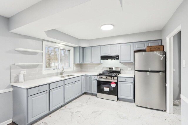 kitchen featuring marble finish floor, stainless steel appliances, gray cabinetry, a sink, and under cabinet range hood