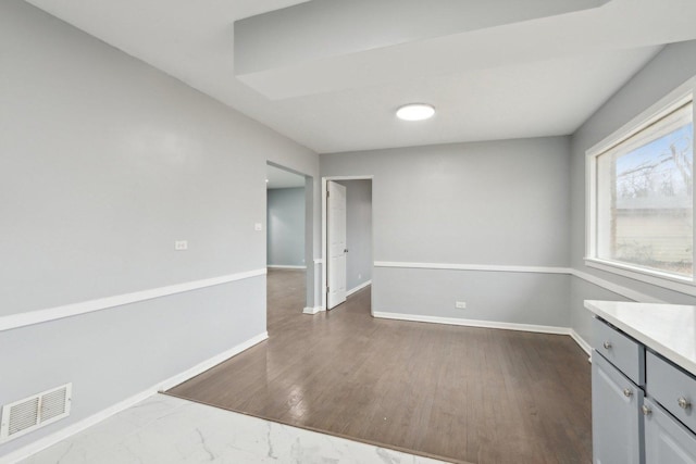 unfurnished room featuring dark wood-type flooring, visible vents, and baseboards