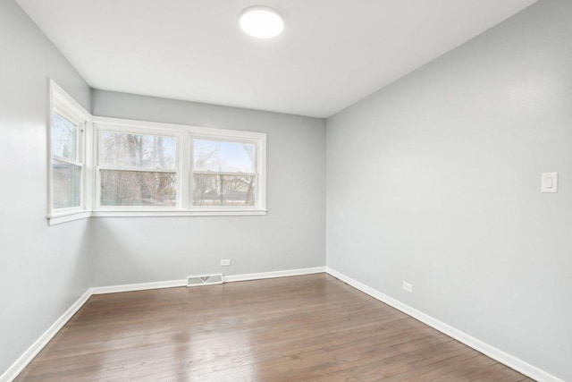 spare room featuring baseboards, visible vents, and wood finished floors