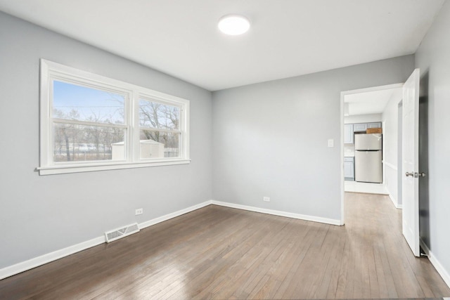 spare room with hardwood / wood-style floors, visible vents, and baseboards