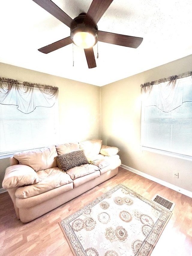 living room with a ceiling fan, baseboards, visible vents, and wood finished floors