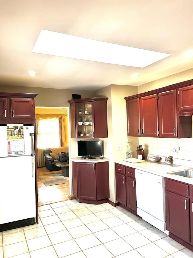 kitchen with light countertops, freestanding refrigerator, a sink, dark brown cabinets, and dishwashing machine