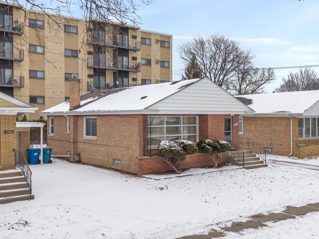 snow covered back of property featuring brick siding and a chimney