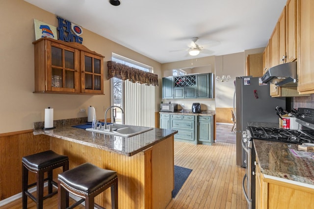 kitchen with a kitchen breakfast bar, a peninsula, under cabinet range hood, stainless steel range with gas cooktop, and a sink