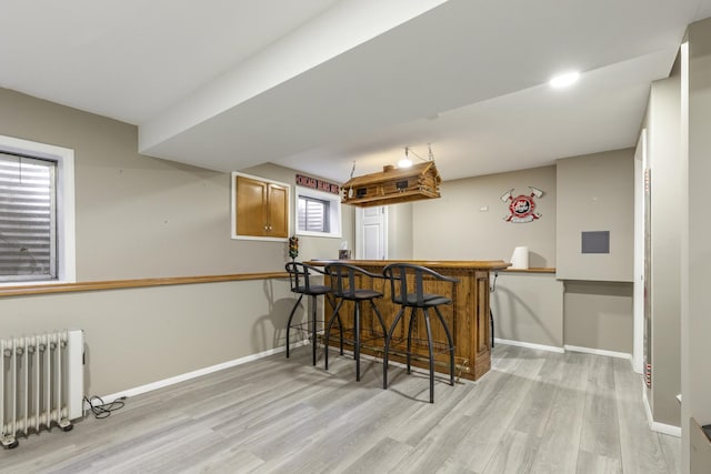 bar with a dry bar, radiator heating unit, light wood-style floors, and baseboards