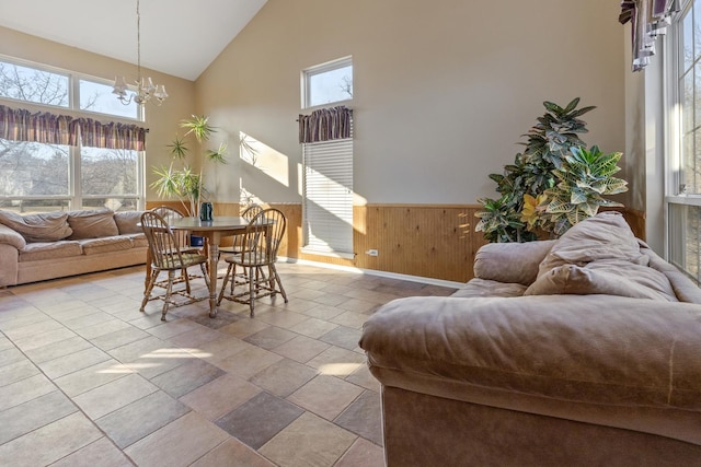 dining room with high vaulted ceiling, wood walls, wainscoting, and an inviting chandelier