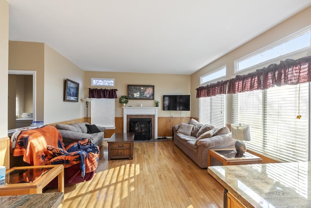 living room featuring a fireplace with flush hearth, light wood-type flooring, and wainscoting