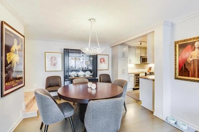 dining area with a chandelier, beverage cooler, baseboards, and ornamental molding