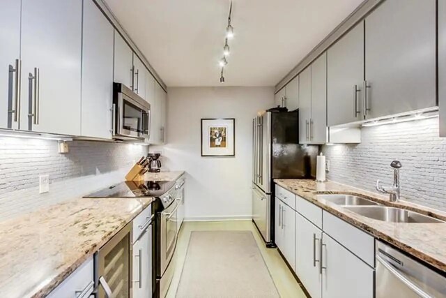 kitchen with backsplash, light stone counters, appliances with stainless steel finishes, and a sink