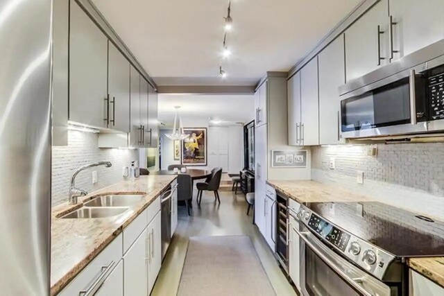 kitchen with light stone counters, gray cabinets, a sink, appliances with stainless steel finishes, and backsplash