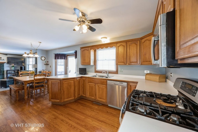 kitchen featuring brown cabinets, a peninsula, light wood-style floors, stainless steel appliances, and a sink