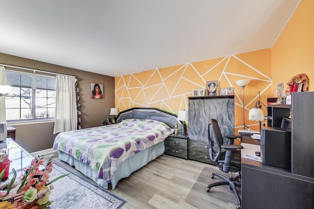 bedroom with an accent wall and wood finished floors