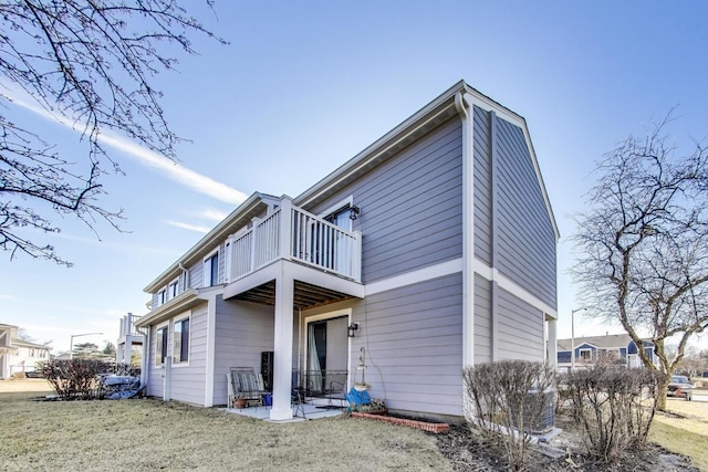 rear view of property featuring a patio area, a lawn, and a balcony