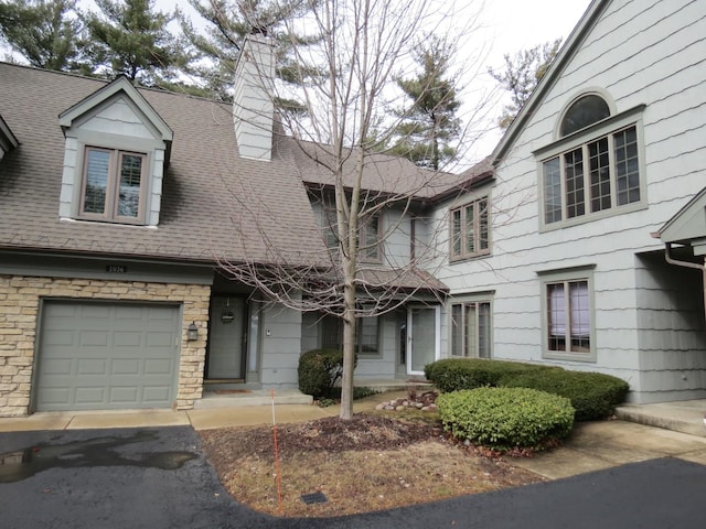 multi unit property with roof with shingles, a chimney, and an attached garage